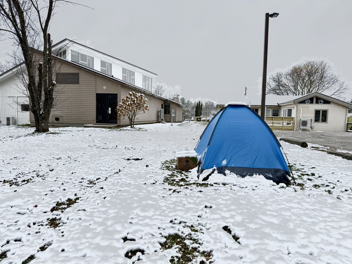 A single tent pitched in fresh snow beside a community building on an overcast Vermont morning